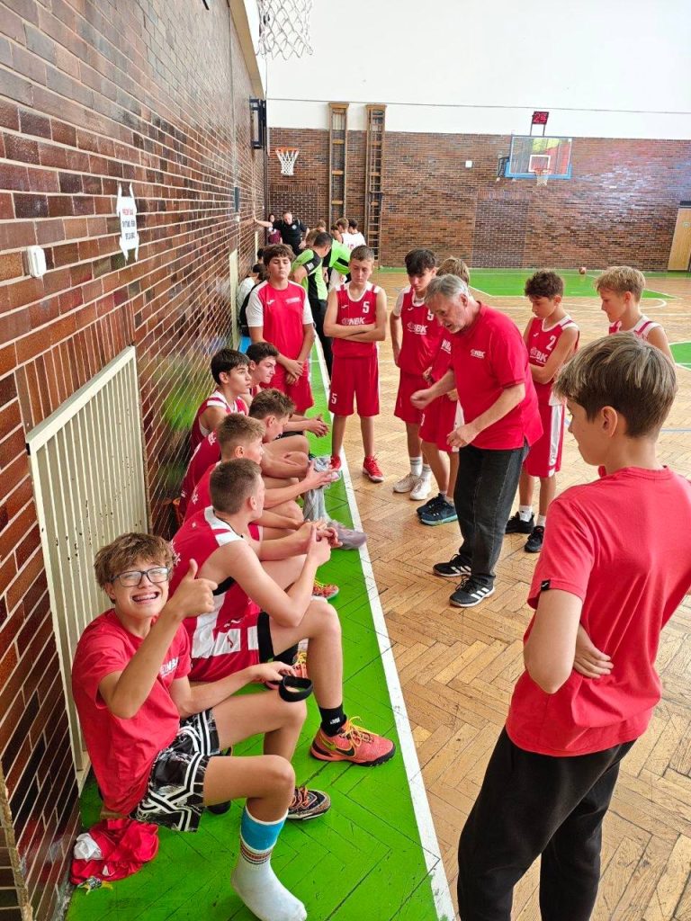 Trenér BA Nymburk U15 udílí pokyny hráčům během pauzy u lavičky v hale v Hradci Králové.