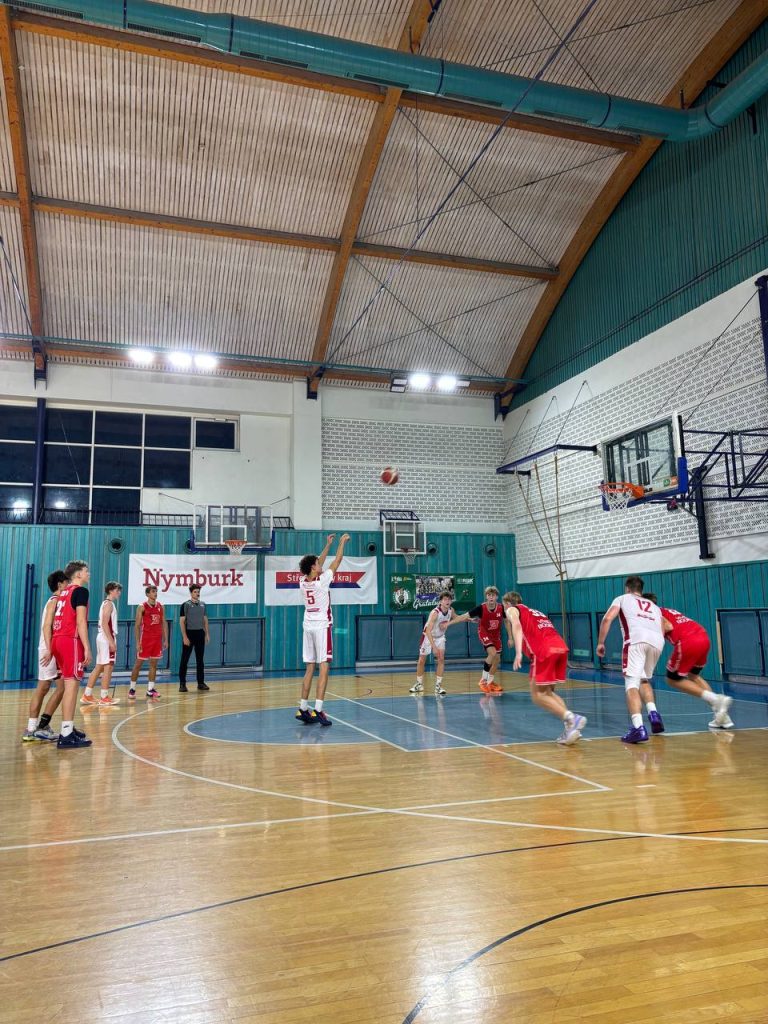 Basketbalový zápas BA Nymburk U17 proti BK VIVIDBOOKS Pardubice v hale na ZŠ Komenského v Nymburku, hráč domácích právě zakončuje z prostoru za trojkovým obloukem.